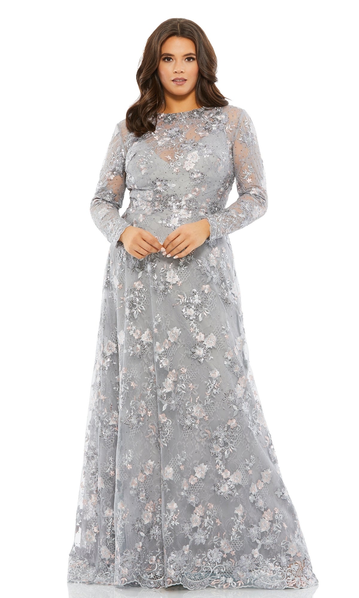 A woman stands facing forward in the Long Plus-Size Formal Dress 67923 by Mac Duggal—a long sleeve platinum lace dress with a v-neck and sheer light gray floral embroidery.